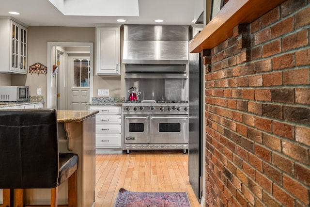 kitchen featuring stainless steel appliances, brick wall, light stone countertops, light wood-type flooring, and white cabinets