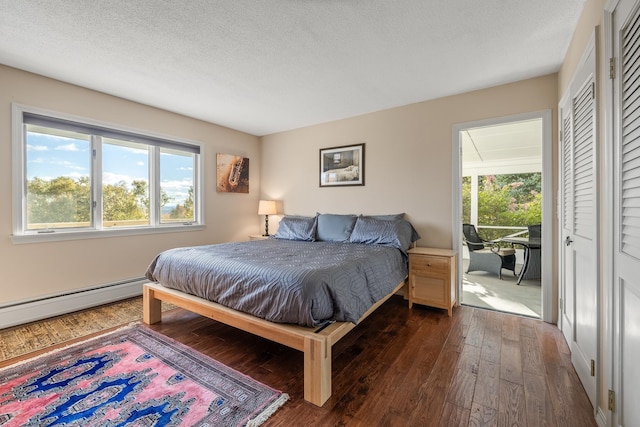 bedroom with a textured ceiling, baseboard heating, and dark wood-type flooring