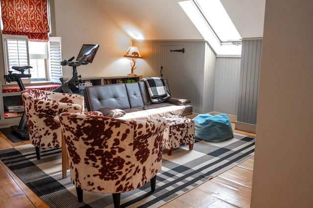 living room featuring light hardwood / wood-style floors, wood walls, and vaulted ceiling with skylight