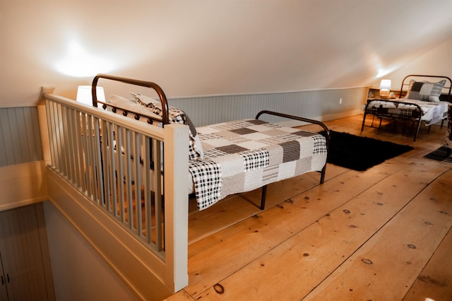 bedroom featuring wooden walls, vaulted ceiling, and light hardwood / wood-style floors