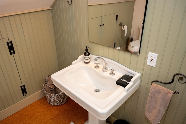 bathroom featuring toilet, wooden walls, and sink