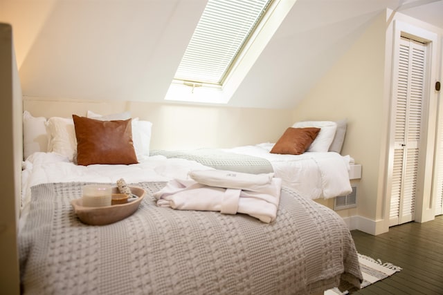 bedroom with lofted ceiling with skylight, dark hardwood / wood-style floors, and a closet