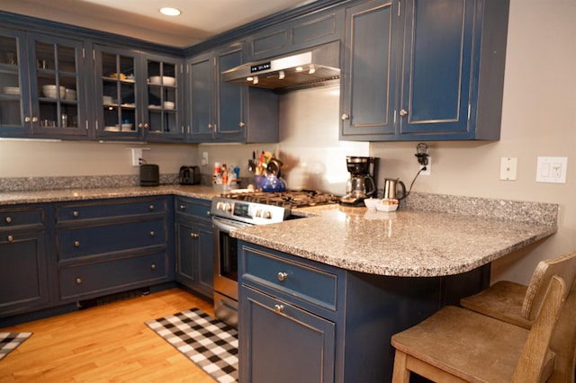 kitchen featuring a breakfast bar area, exhaust hood, high end range, light wood-type flooring, and blue cabinetry