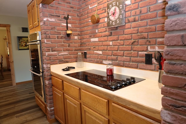 kitchen featuring black electric stovetop, dark hardwood / wood-style floors, brick wall, and stainless steel double oven