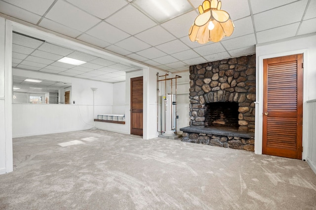 unfurnished living room with a paneled ceiling, a stone fireplace, and carpet flooring