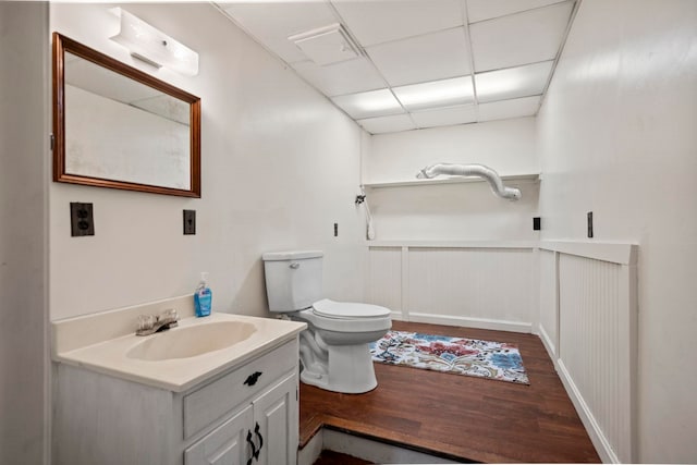 bathroom with toilet, a drop ceiling, hardwood / wood-style floors, and vanity