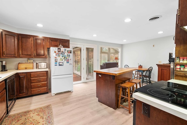 kitchen featuring a kitchen island, a kitchen breakfast bar, range, white fridge, and light hardwood / wood-style floors