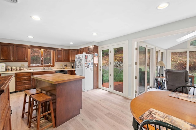 kitchen with a kitchen bar, light hardwood / wood-style flooring, lofted ceiling with skylight, wooden counters, and white appliances