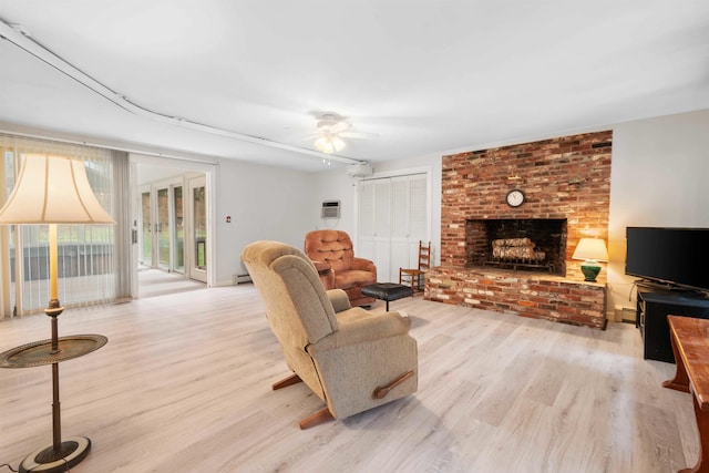 living room with a wall unit AC, a baseboard radiator, ceiling fan, a brick fireplace, and light hardwood / wood-style flooring