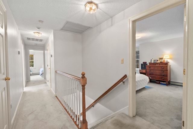 hall featuring a textured ceiling, baseboard heating, and light colored carpet