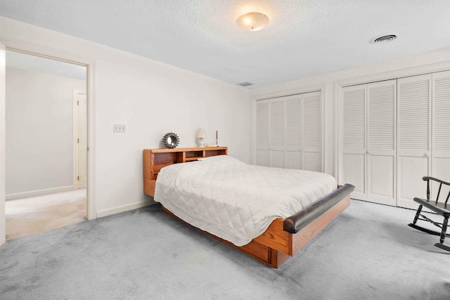 bedroom featuring multiple closets, a textured ceiling, and light colored carpet