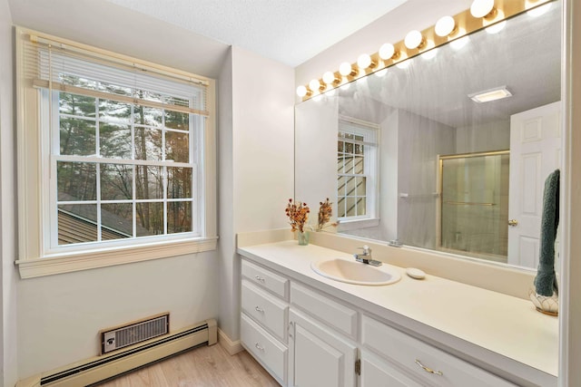 bathroom with a shower with door, hardwood / wood-style flooring, a baseboard heating unit, vanity, and a textured ceiling