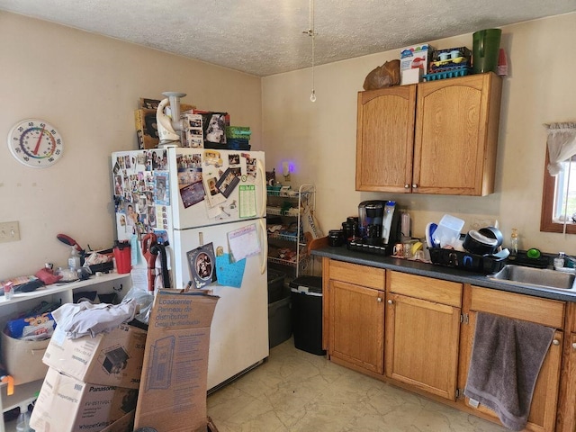 kitchen featuring white refrigerator, sink, and a textured ceiling