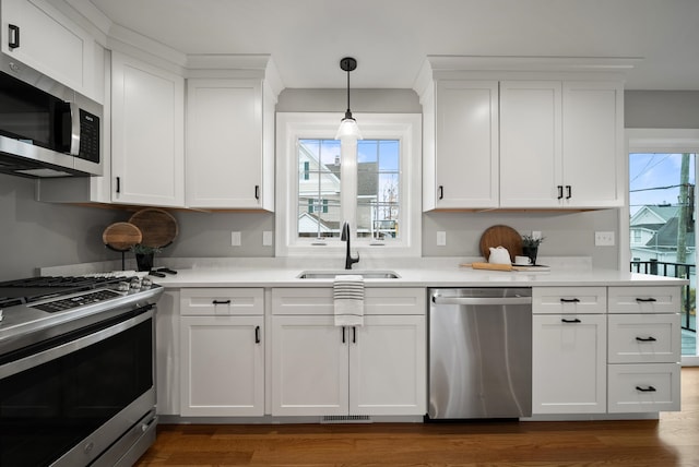 kitchen with appliances with stainless steel finishes, dark hardwood / wood-style floors, white cabinets, and sink