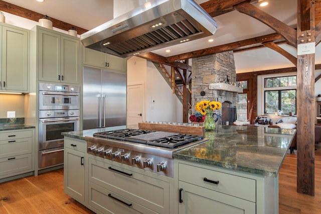 kitchen with island range hood, dark stone countertops, green cabinetry, appliances with stainless steel finishes, and light hardwood / wood-style floors