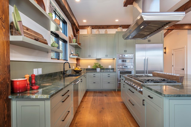 kitchen with appliances with stainless steel finishes, sink, island range hood, light hardwood / wood-style floors, and dark stone countertops