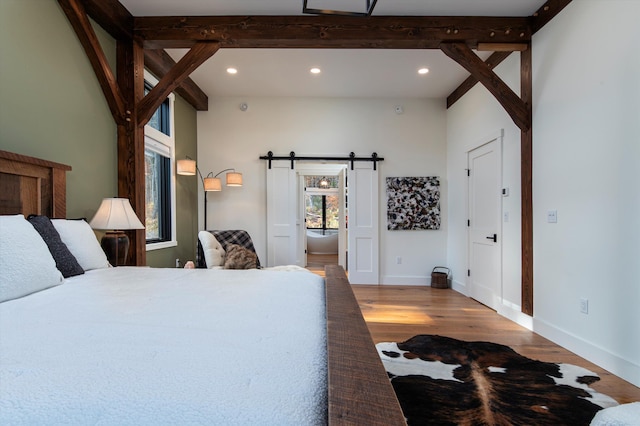 bedroom with beam ceiling, a barn door, and wood-type flooring