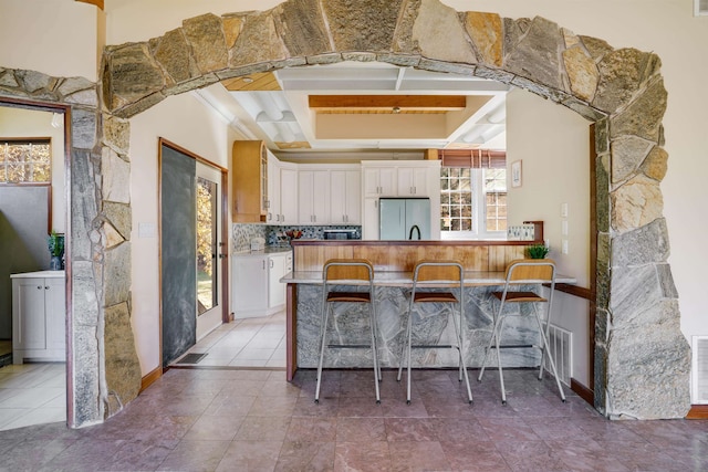 kitchen featuring a breakfast bar, white cabinetry, beam ceiling, and stainless steel refrigerator