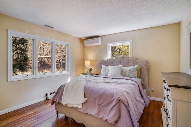 bedroom with a wall mounted air conditioner, a baseboard heating unit, a textured ceiling, and wood-type flooring