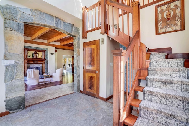 stairway with beam ceiling, a stone fireplace, and wooden ceiling