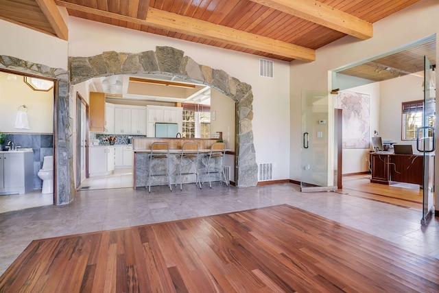 kitchen with wood ceiling, a kitchen breakfast bar, white cabinetry, light hardwood / wood-style flooring, and beamed ceiling