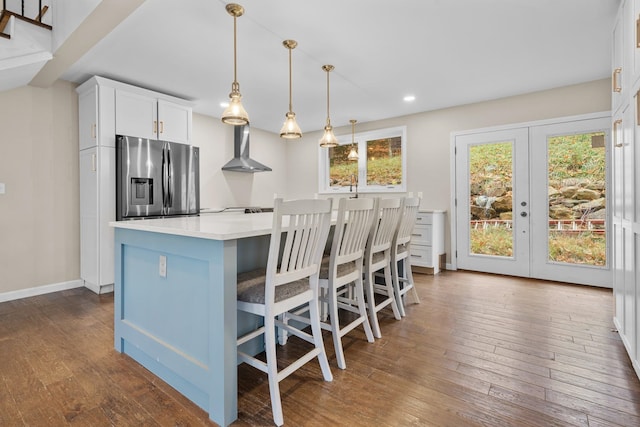 kitchen featuring wall chimney range hood, stainless steel fridge with ice dispenser, white cabinetry, pendant lighting, and a center island