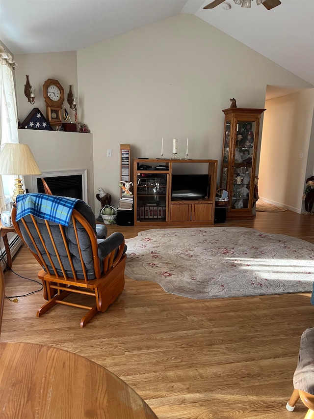 living room with ceiling fan, a baseboard heating unit, wood-type flooring, and vaulted ceiling