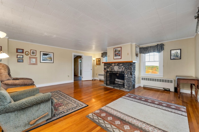 living room with a stone fireplace, radiator, hardwood / wood-style flooring, and ornamental molding