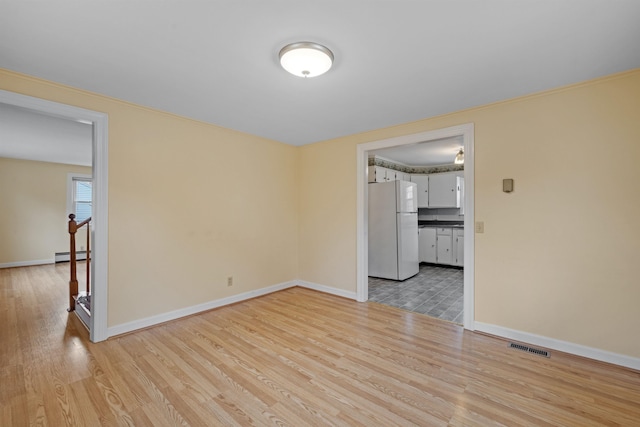 spare room featuring a baseboard heating unit and light wood-type flooring