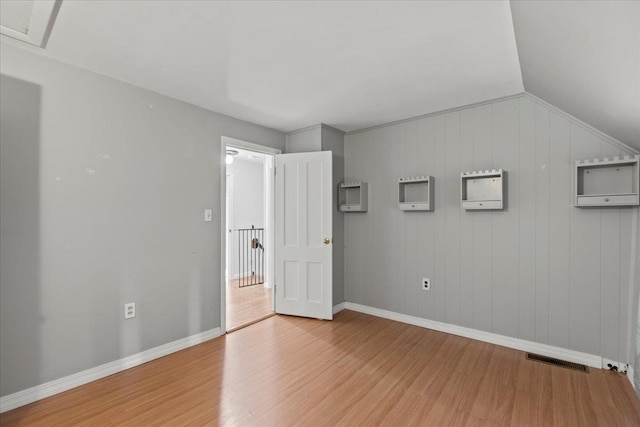 unfurnished bedroom with hardwood / wood-style floors, wooden walls, and vaulted ceiling