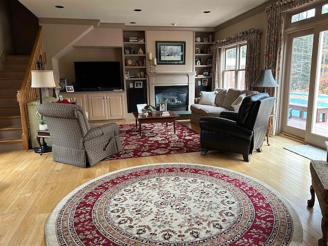 living room featuring light hardwood / wood-style floors, crown molding, and built in shelves