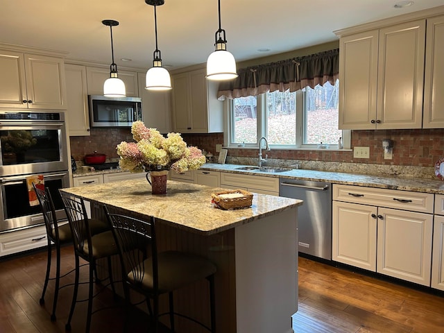 kitchen with appliances with stainless steel finishes, dark hardwood / wood-style floors, light stone countertops, sink, and a center island