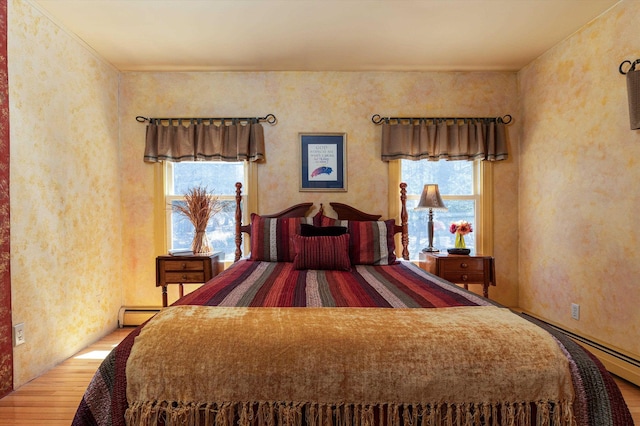 bedroom featuring baseboard heating, multiple windows, and wood finished floors