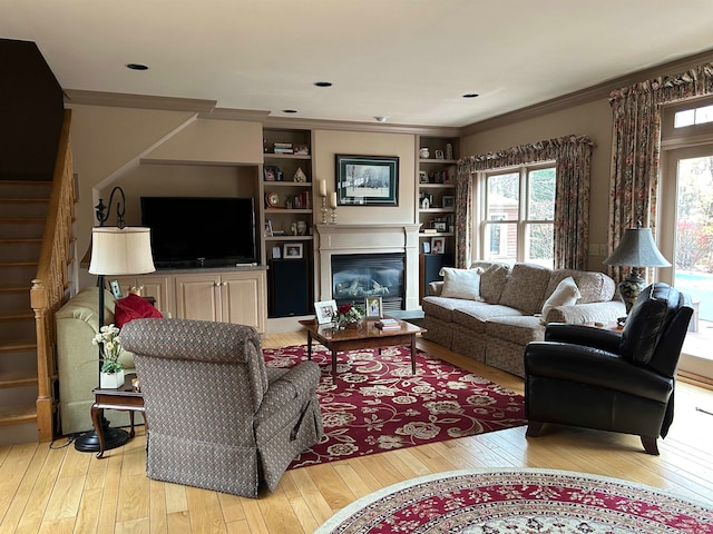 living room featuring a wealth of natural light, light hardwood / wood-style flooring, built in shelves, and ornamental molding