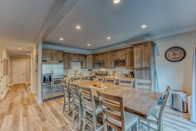 kitchen featuring tasteful backsplash, ornamental molding, light wood-type flooring, appliances with stainless steel finishes, and sink