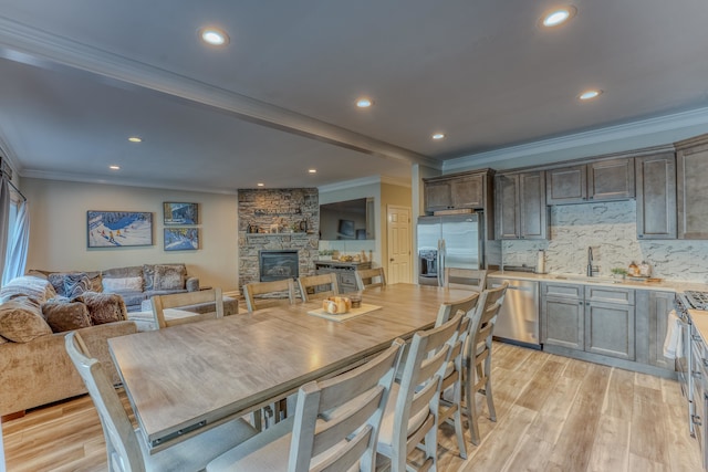 dining room with sink, a stone fireplace, light wood-type flooring, and crown molding