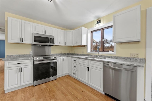 kitchen featuring light stone countertops, sink, light hardwood / wood-style floors, white cabinets, and appliances with stainless steel finishes