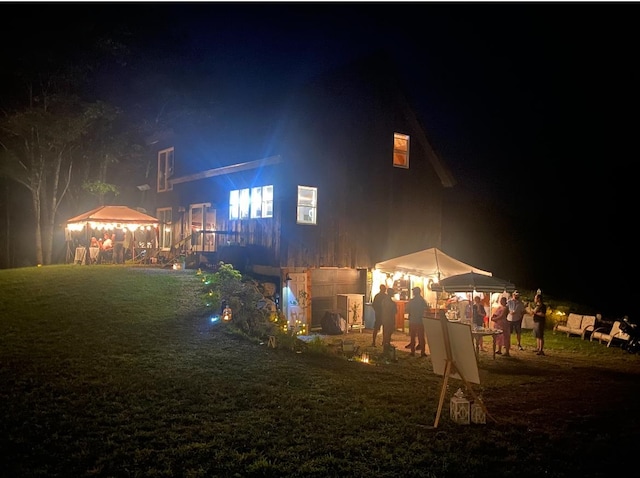 back house at twilight with a gazebo and a yard