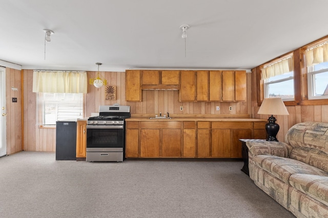 kitchen with wood walls, light carpet, sink, stainless steel range with gas cooktop, and pendant lighting