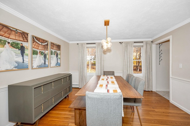 dining space with a baseboard heating unit, light wood-type flooring, crown molding, and a notable chandelier