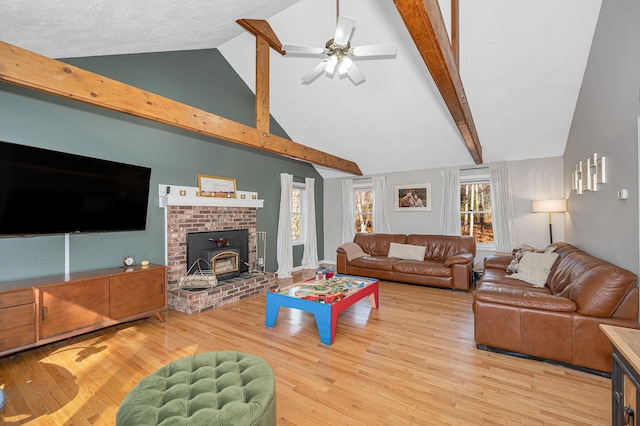 living room featuring a brick fireplace, light hardwood / wood-style flooring, beamed ceiling, and ceiling fan