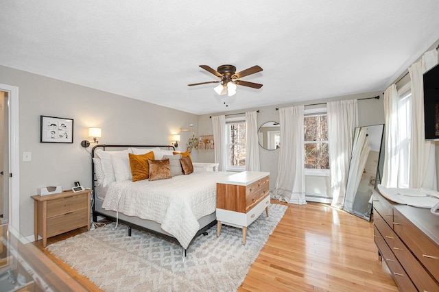 bedroom with a baseboard heating unit, light hardwood / wood-style floors, and ceiling fan