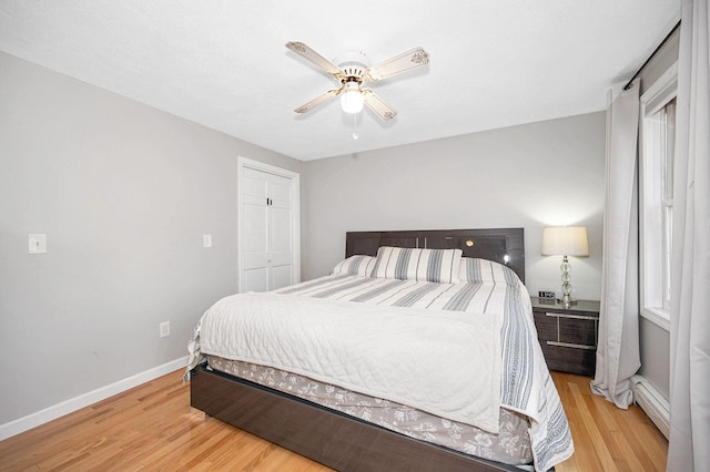 bedroom featuring a baseboard heating unit, light hardwood / wood-style floors, ceiling fan, and a closet