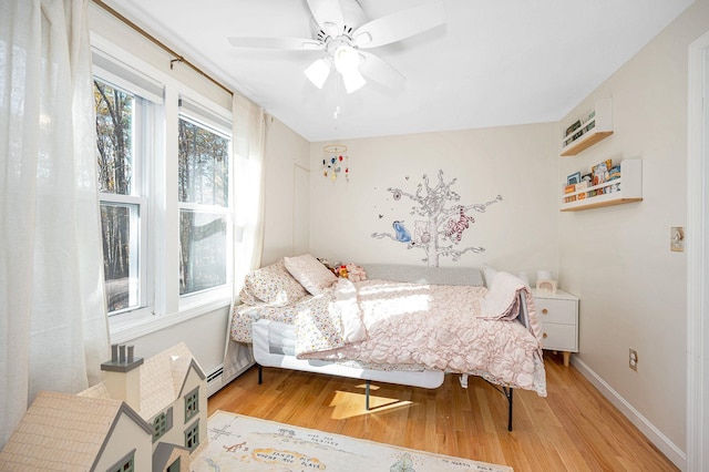 bedroom with ceiling fan, light hardwood / wood-style floors, and a baseboard heating unit