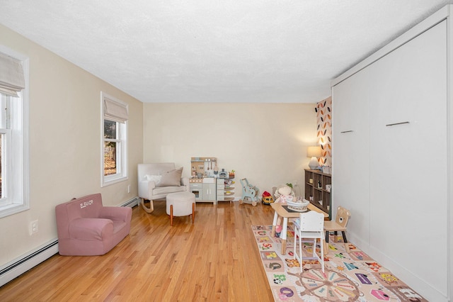 living area featuring light wood-type flooring, baseboard heating, and plenty of natural light