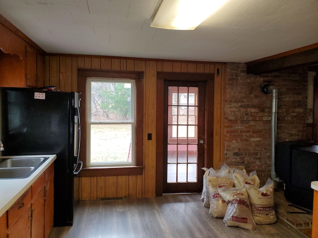 interior space featuring sink, black fridge, wood-type flooring, a wood stove, and wooden walls