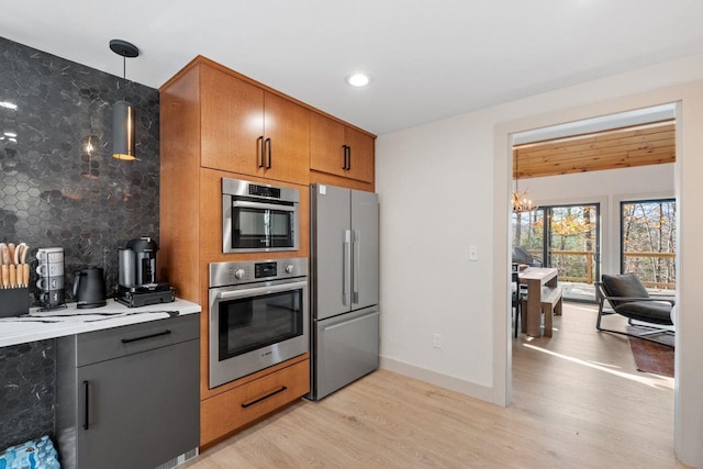 kitchen featuring stainless steel appliances, tasteful backsplash, decorative light fixtures, and light hardwood / wood-style flooring