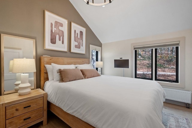 bedroom with radiator heating unit, wood-type flooring, and lofted ceiling