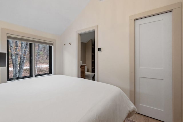 bedroom featuring ensuite bath, hardwood / wood-style flooring, vaulted ceiling, and a closet