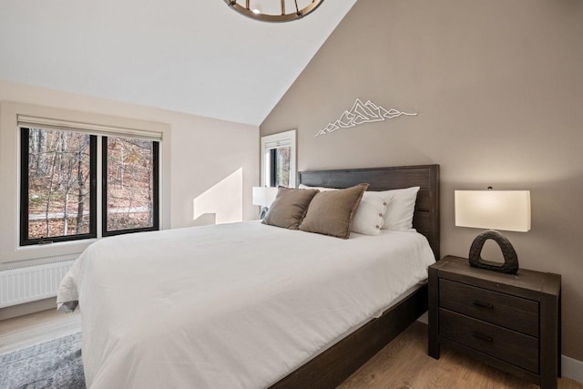 bedroom with light wood-type flooring, lofted ceiling, and radiator